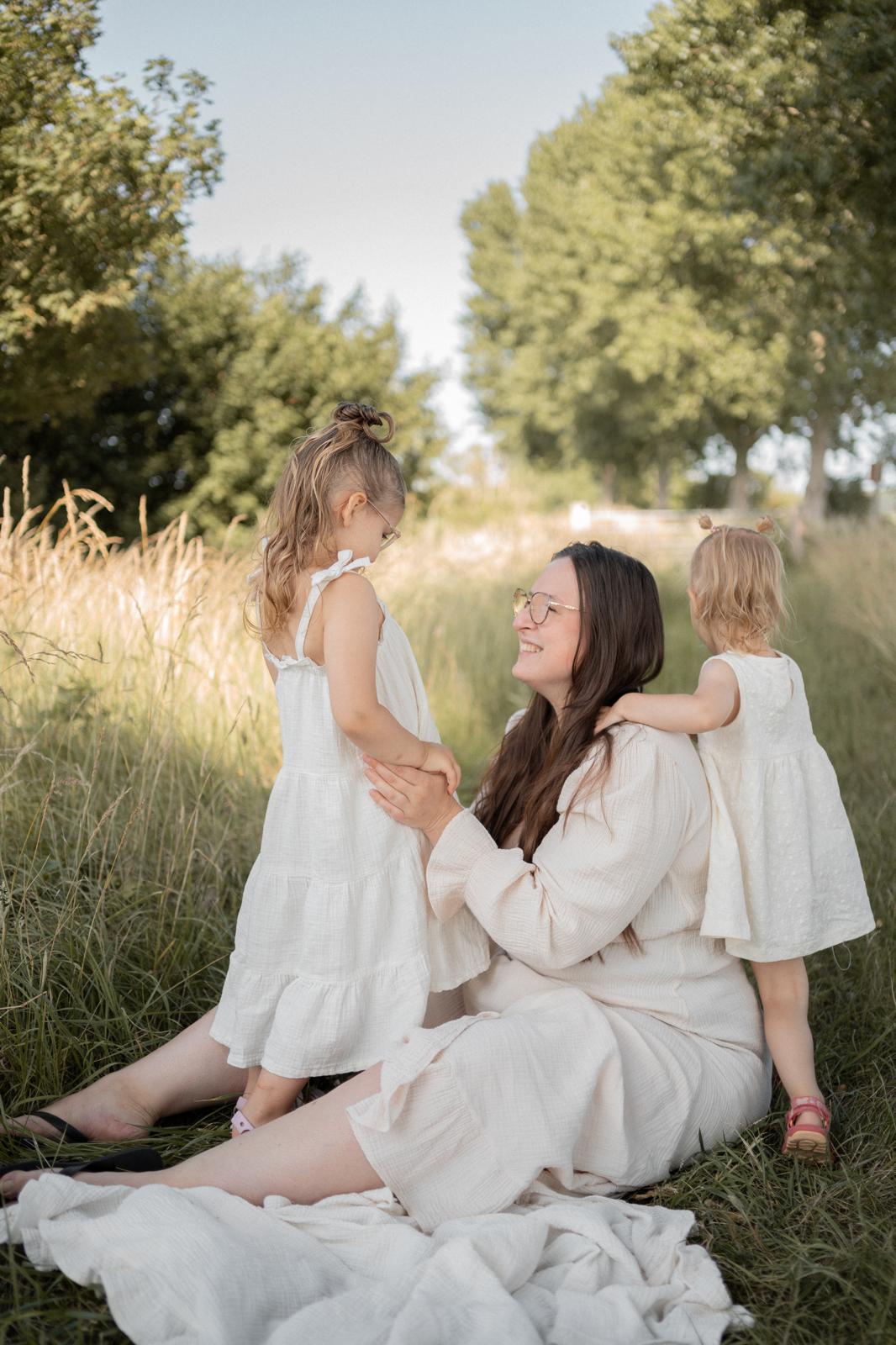 Aniek samen met haar twee dochters in het gras tijdens een liefdevol moment buiten, een warm beeld dat het echte leven met dochters laat zien.